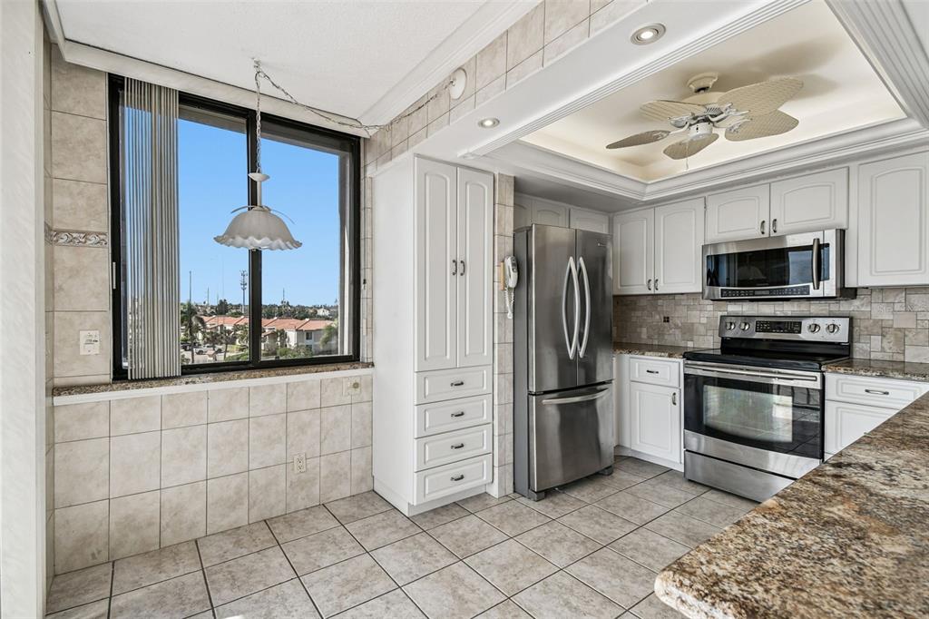 A kitchen with white cabinets, stainless steel appliances, tiled walls, and a large window — 6104 PALMA DEL MAR BOULEVARD S UNIT 402, ST PETERSBURG, FL