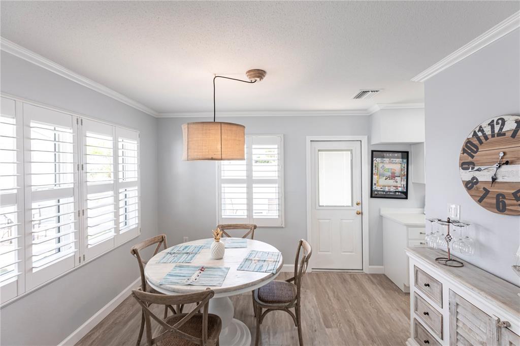 A dining room features a round white table, wooden chairs, plantation shutters, and a wall clock — 6020 MIDNIGHT PASS ROAD UNIT 30, SARASOTA, FL