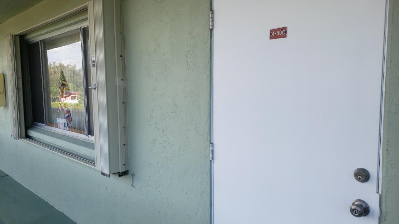A white door labeled M-306 sits next to a window on a light green exterior wall — 3300 Springdale Boulevard # 306, Palm Springs FL 33461, PALM SPRINGS, FL