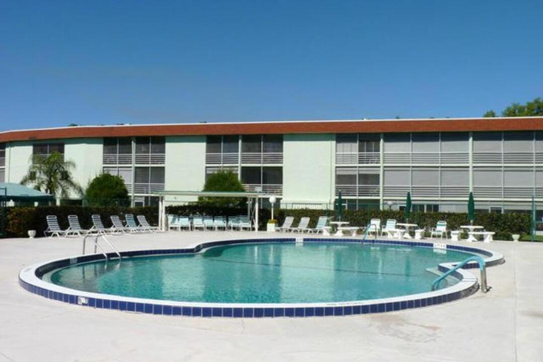 A kidney-shaped swimming pool sits on a concrete deck in front of a multi-story building — 3300 Springdale Boulevard # 306, Palm Springs FL 33461, PALM SPRINGS, FL