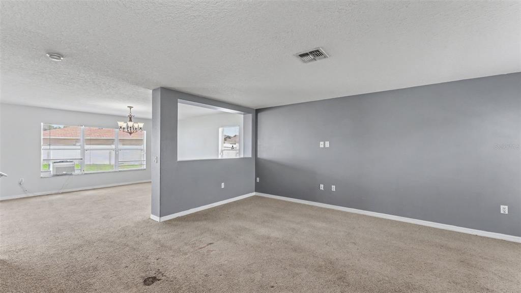 A living room with beige carpet, gray walls, and a large rectangular cutout in the wall — 3014 YARROW LANE, MULBERRY, FL