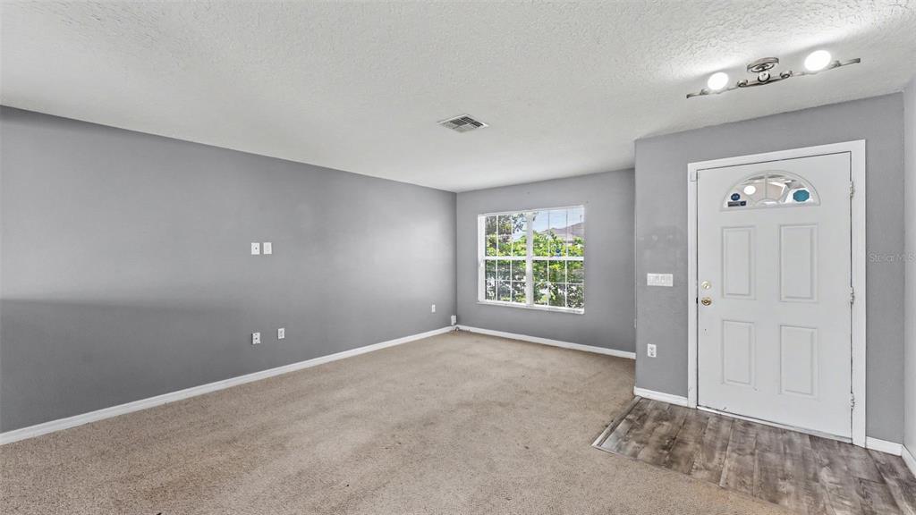 An empty living room features gray walls, beige carpeting, a window, and a white door — 3014 YARROW LANE, MULBERRY, FL