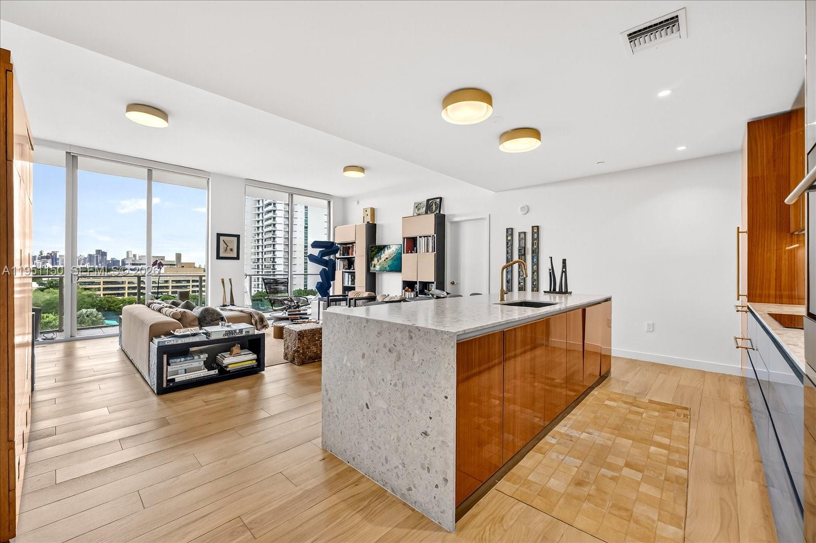A modern kitchen with a stone island and wood cabinetry overlooks a bright living area — 2678 Tigertail Ave # 604, Miami FL 33133, MIAMI, FL