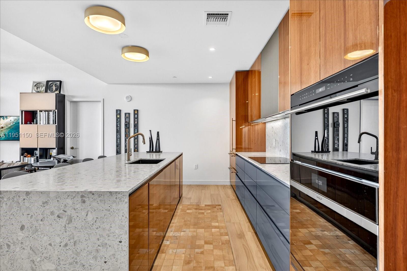 A modern kitchen features a stone-topped island, wood-toned cabinetry, and dark blue lower cabinets — 2678 Tigertail Ave # 604, Miami FL 33133, MIAMI, FL