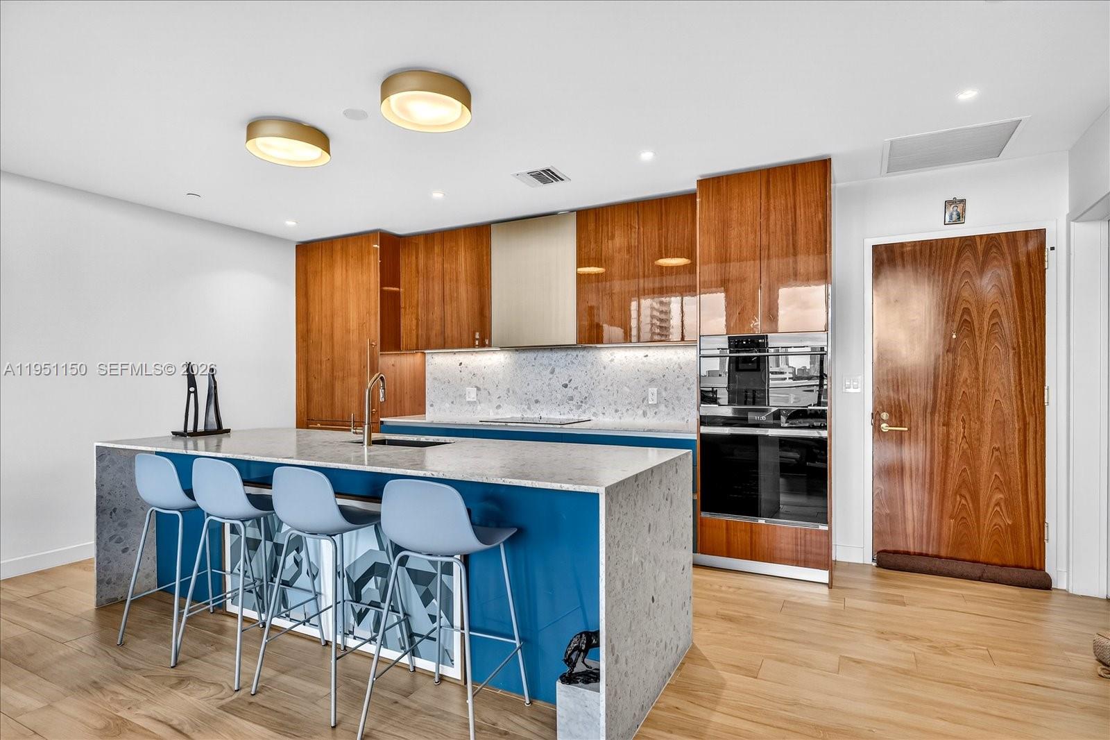 A modern kitchen features blue cabinetry, a stone island, and wood-toned upper cabinets — 2678 Tigertail Ave # 604, Miami FL 33133, MIAMI, FL