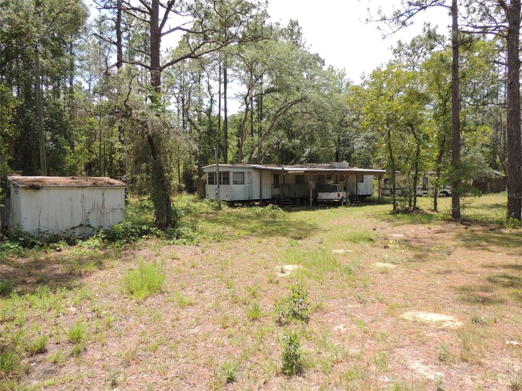 A mobile home with a covered carport sits on a wooded lot with a shed — 250 NE 131ST AVENUE, WILLISTON, FL