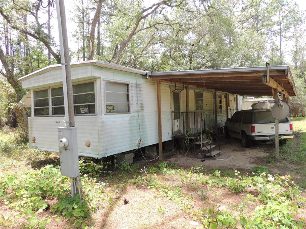 An exterior view of an aged mobile home with a carport and a parked SUV — 250 NE 131ST AVENUE, WILLISTON, FL