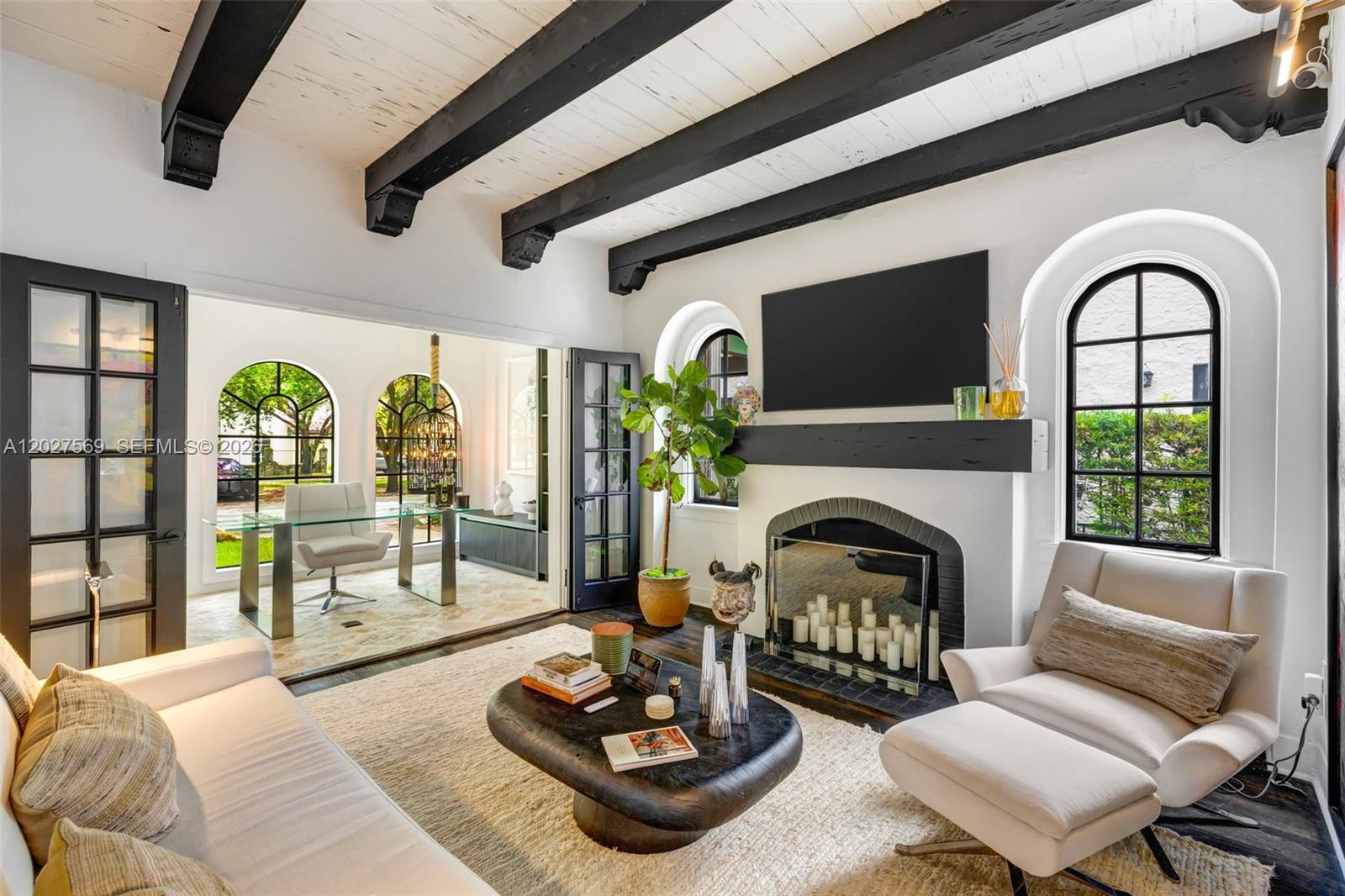 A living room features exposed black ceiling beams, a fireplace, and arched windows — 1225 Alhambra Cir, Coral Gables FL 33134, CORAL GABLES, FL