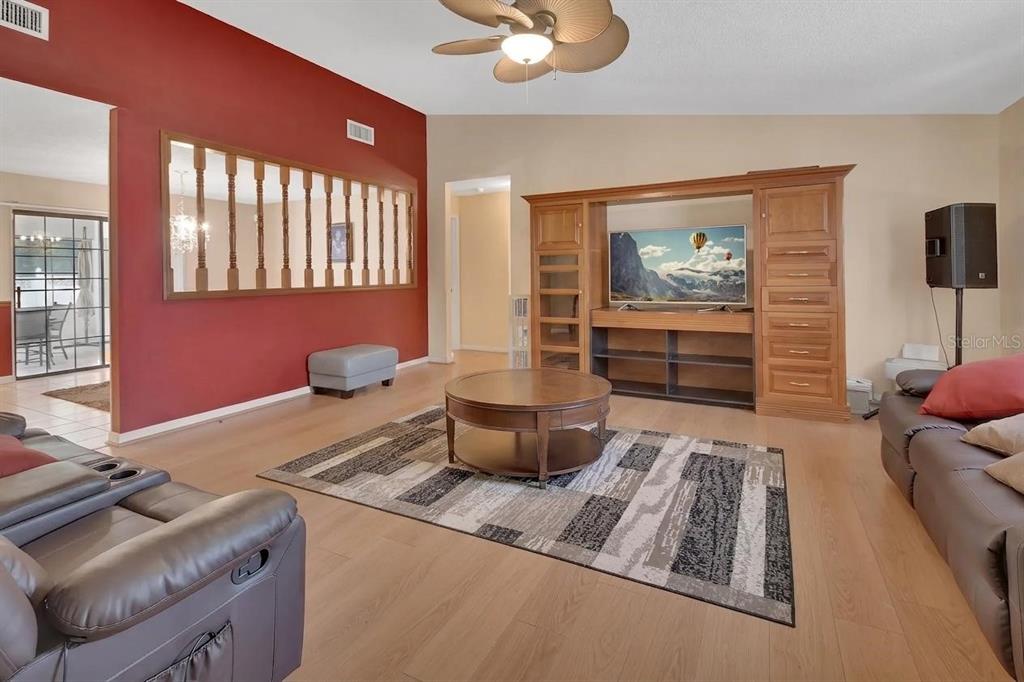 A living room with light wood floors, a red accent wall, and a wooden entertainment center — 7330 SE 109TH PLACE, BELLEVIEW, FL