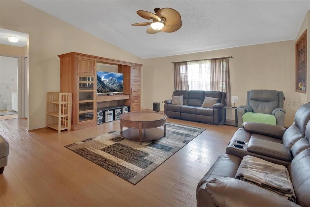 A living room features wood-look flooring, a large entertainment center, and leather furniture — 7330 SE 109TH PLACE, BELLEVIEW, FL
