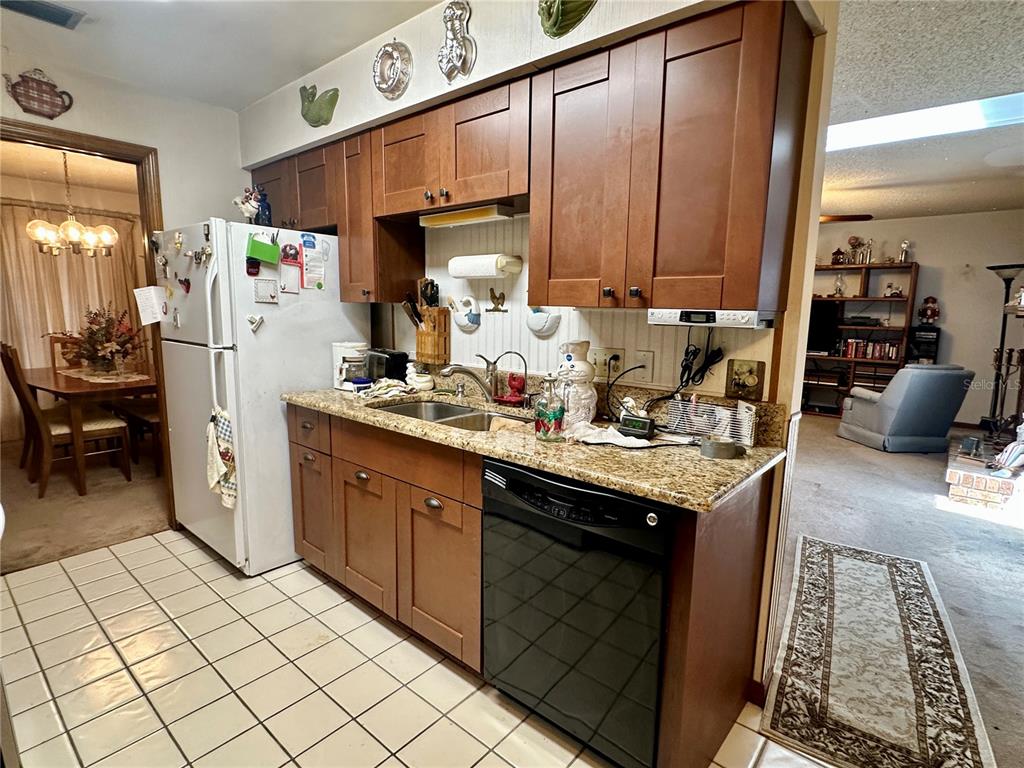 A kitchen features wood cabinets, granite countertops, a black dishwasher, and white tile flooring — 723 GASTON FOSTER ROAD, ORLANDO, FL