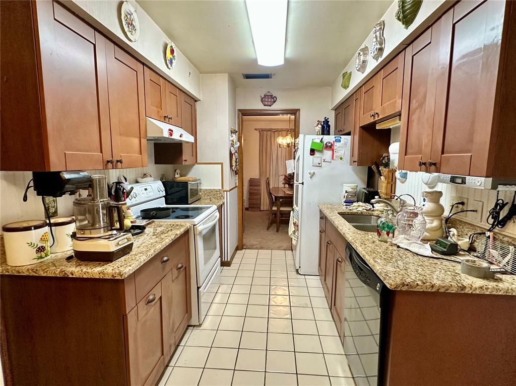 A galley kitchen features wood cabinets, granite countertops, white appliances, and a tiled floor — 723 GASTON FOSTER ROAD, ORLANDO, FL