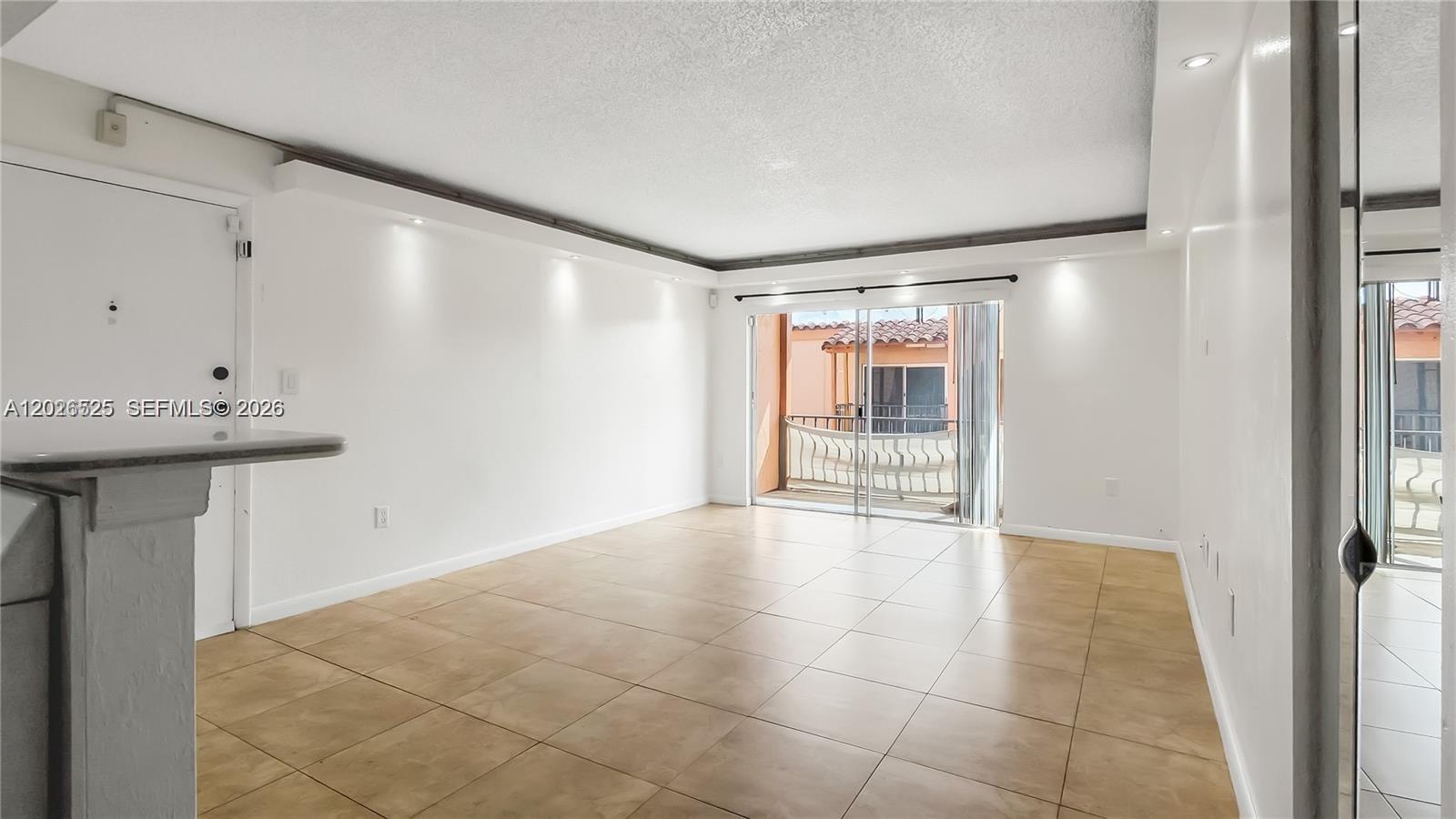 A bright, empty living room features beige tile flooring, recessed lighting, and a sliding glass door — 7200 Fairway Dr # H12, Miami Lakes FL 33014, MIAMI LAKES, FL