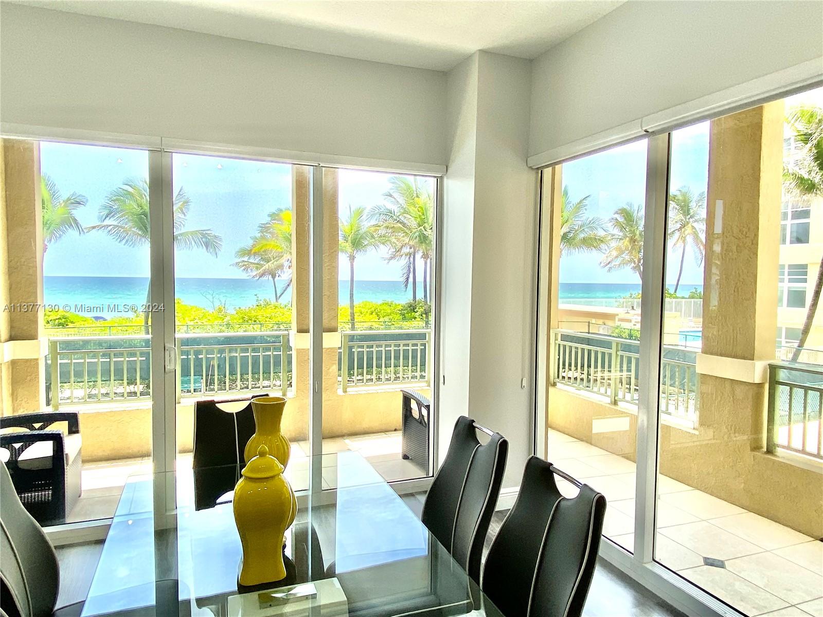 A dining area with a glass table and black chairs overlooks a balcony and ocean — 2080 S Ocean Dr # 111, Hallandale Beach FL 33009, HALLANDALE BEACH, FL