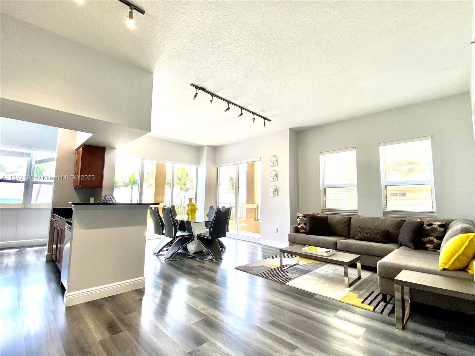 An open-concept living and dining area features gray wood-look flooring and modern track lighting — 2080 S Ocean Dr # 111, Hallandale Beach FL 33009, HALLANDALE BEACH, FL