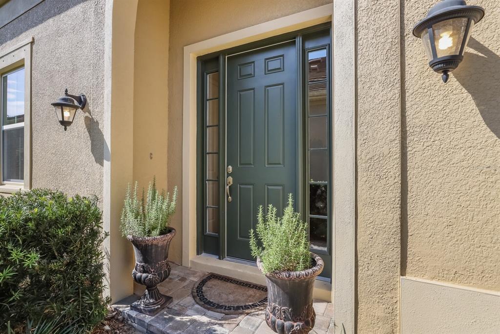 A dark green front door with sidelights is flanked by two potted plants and wall sconces — 2402 STARWOOD COURT, LAKEWOOD RANCH, FL