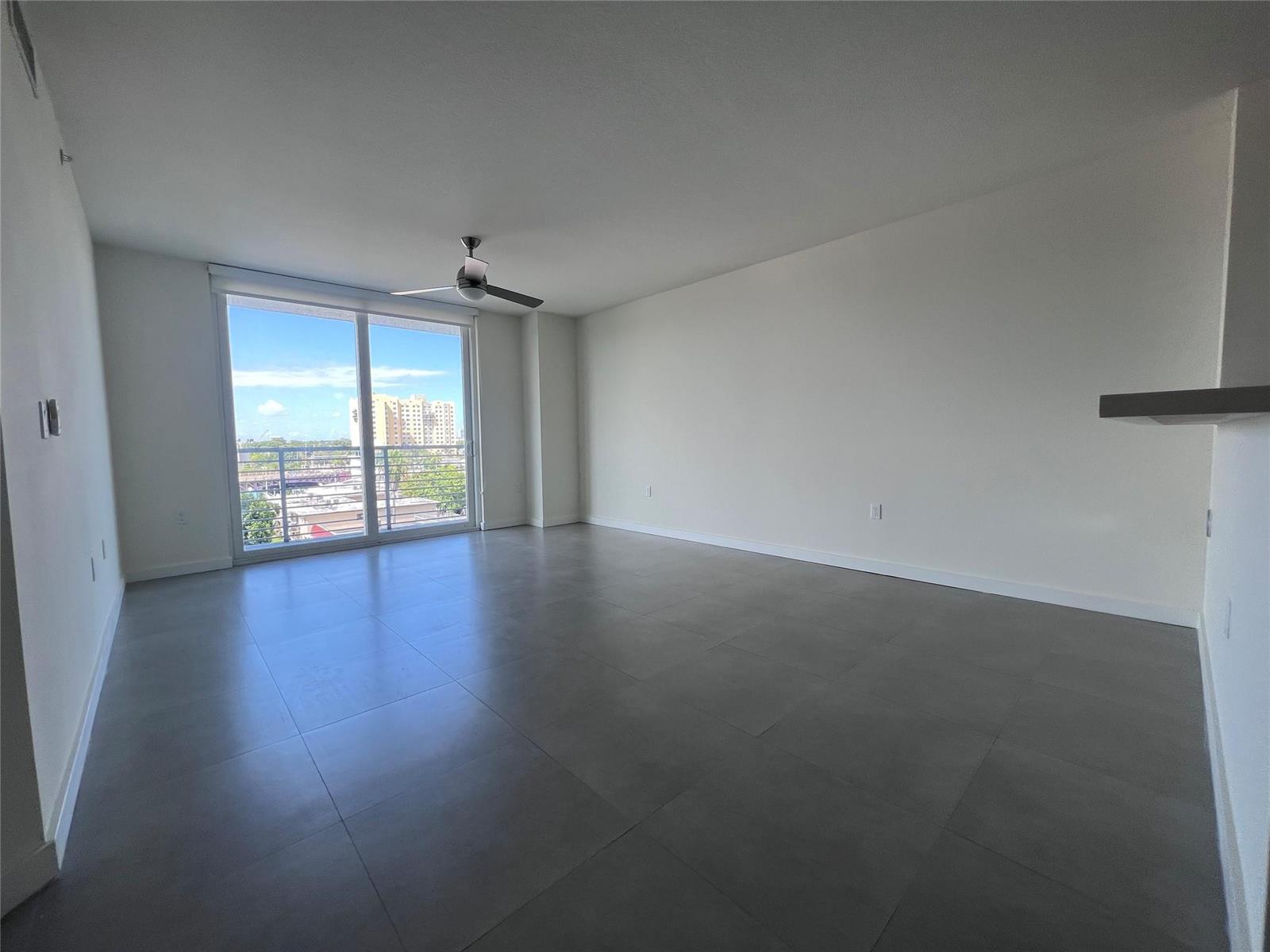 An empty living room features large gray floor tiles, white walls, and a sliding glass door — 729 NW 2 Street # 525, Miami FL 33128, MIAMI, FL