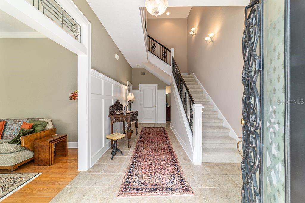 A foyer features a staircase with a black railing, tile flooring, and a long rug — 905 SE 12TH STREET, OCALA, FL