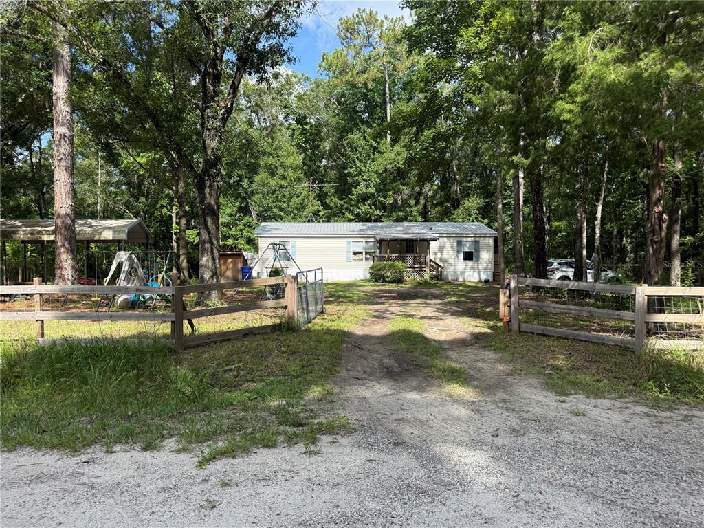 A single-story manufactured home sits behind a wooden fence on a wooded lot — 10225 WEATHERBY AVENUE, HASTINGS, FL