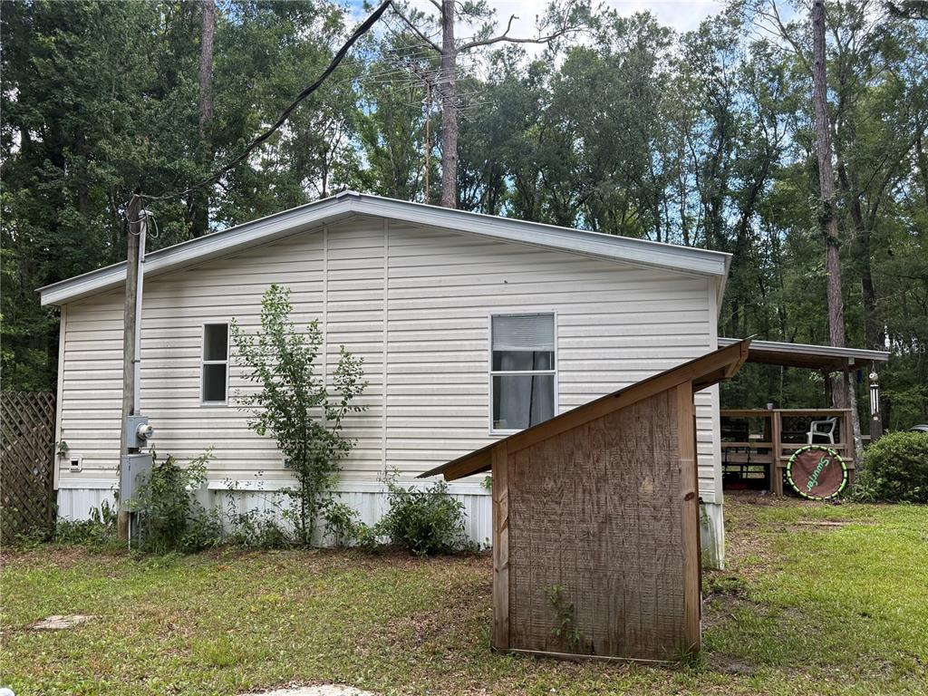 A side view of a light-colored mobile home with a small wooden shed in front — 10225 WEATHERBY AVENUE, HASTINGS, FL