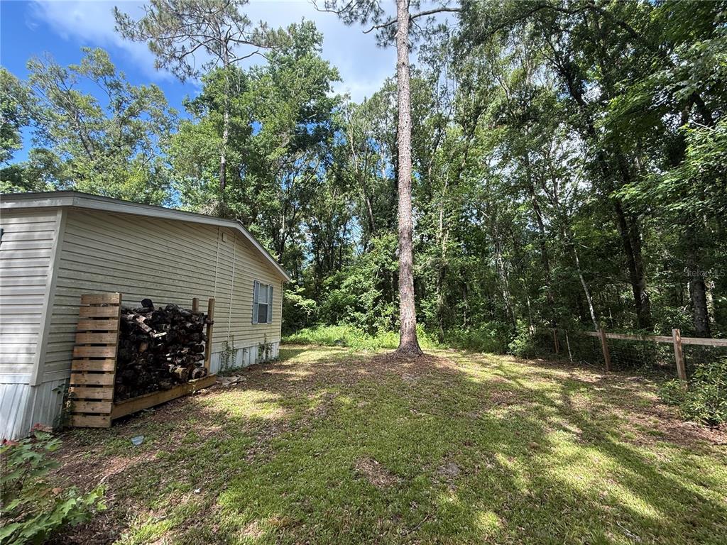 A side view of a mobile home with a wood rack and a wooded backyard — 10225 WEATHERBY AVENUE, HASTINGS, FL