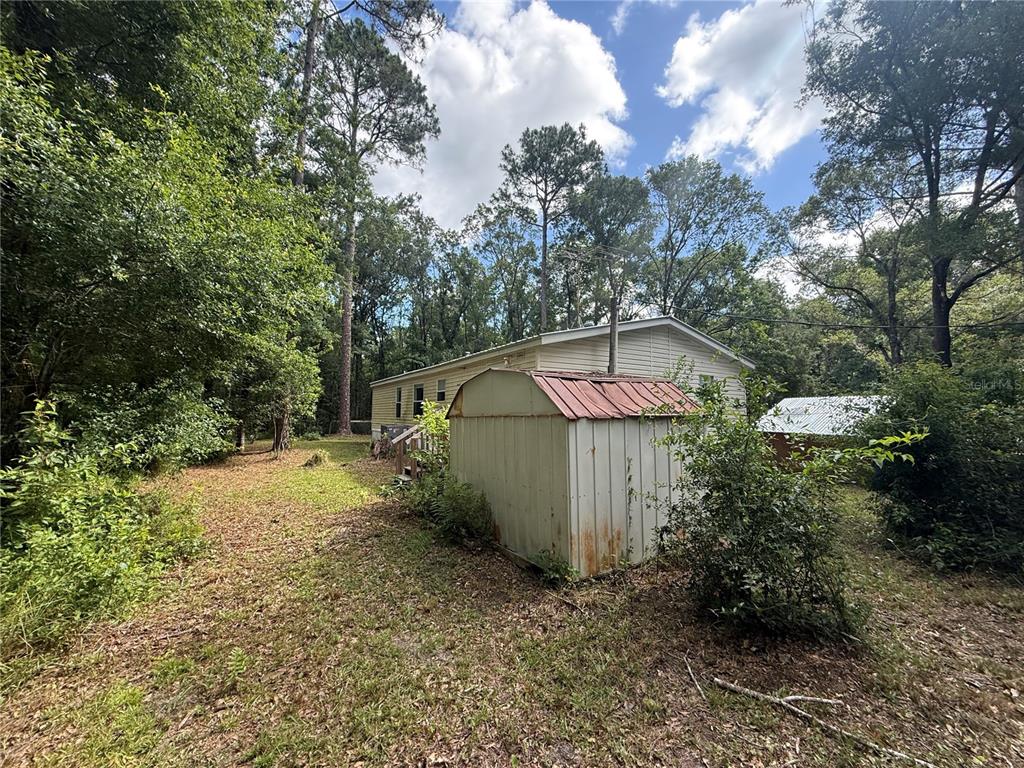 A metal shed sits in a wooded yard in front of a light-colored mobile home — 10225 WEATHERBY AVENUE, HASTINGS, FL