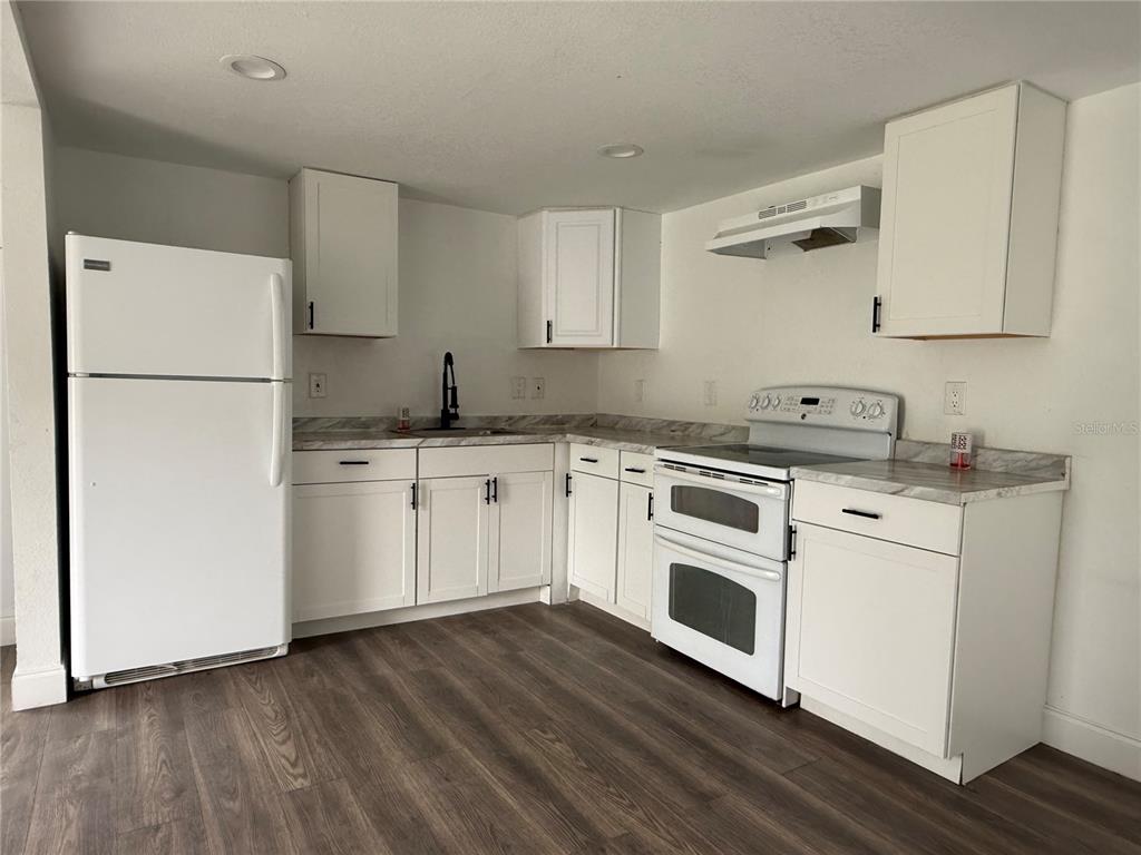 A kitchen with white cabinets, marble-patterned countertops, white appliances, and wood-look flooring — 3931 AVENUE R NW, WINTER HAVEN, FL