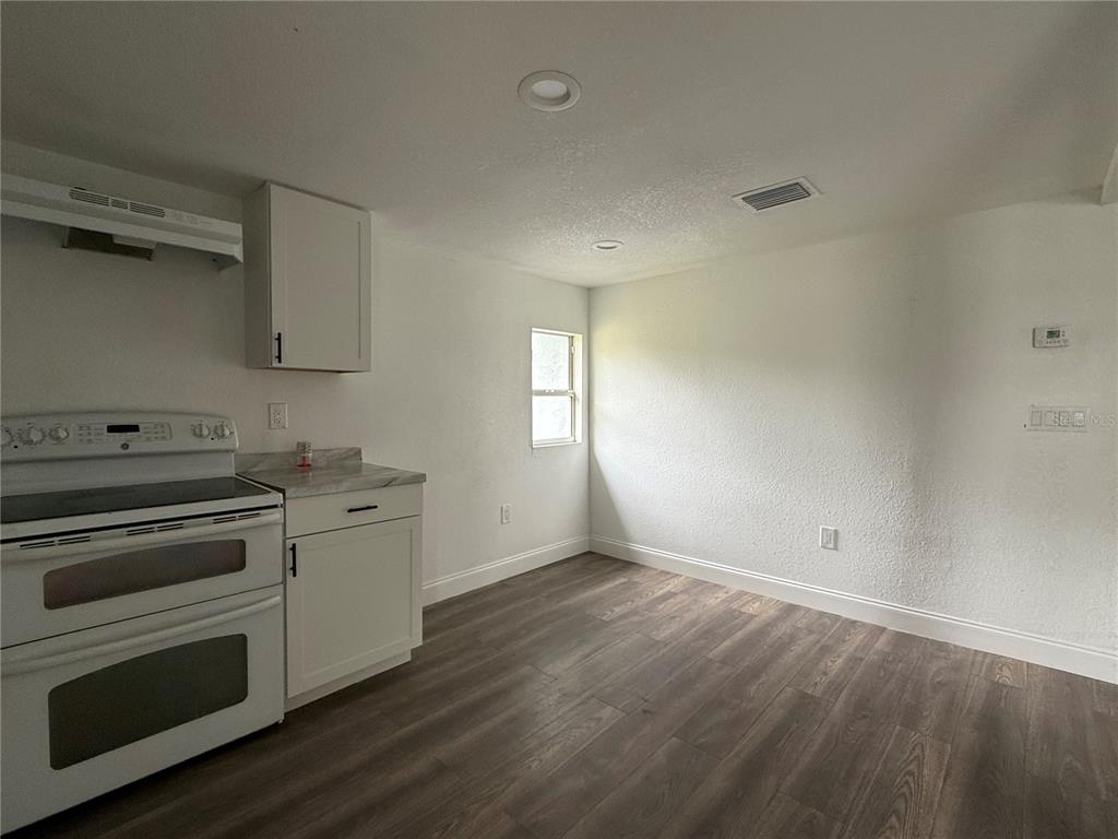 A kitchen area features white cabinets, a white stove, and wood-look flooring — 3931 AVENUE R NW, WINTER HAVEN, FL