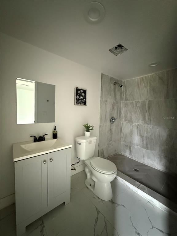A bathroom features a gray vanity, a white toilet, and a walk-in shower with marble-look tile — 3931 AVENUE R NW, WINTER HAVEN, FL
