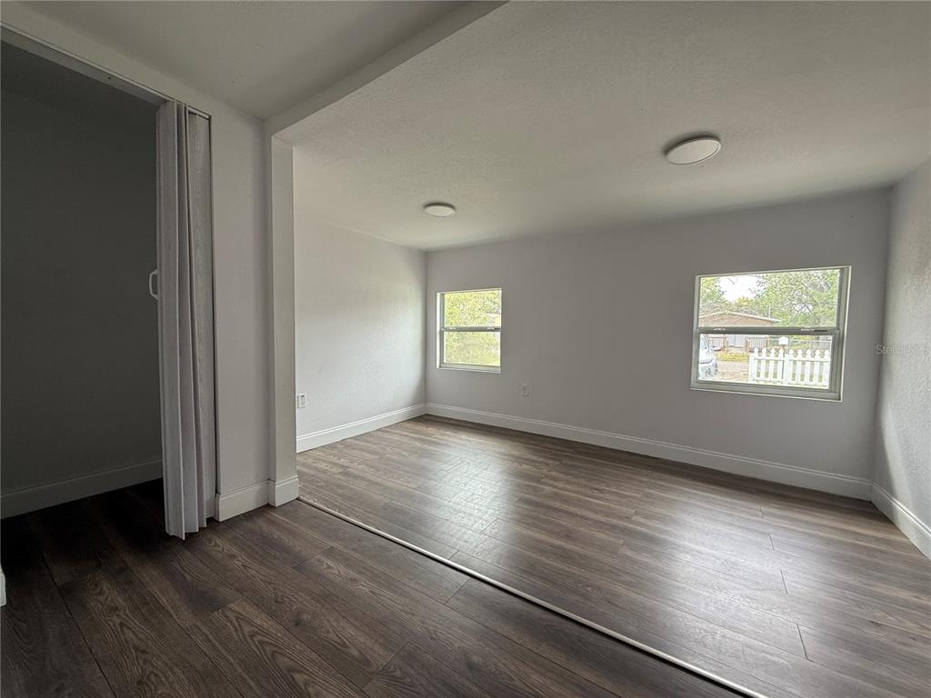 An empty room features wood-look flooring, white walls, two windows, and a folding closet door — 3931 AVENUE R NW, WINTER HAVEN, FL