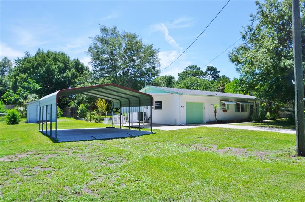 A white house with a green garage door and a detached metal carport in front — 405 S CAMELLIA AVENUE, CRYSTAL RIVER, FL