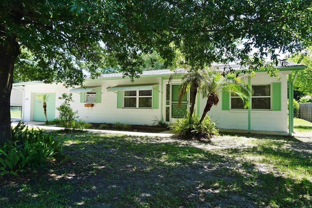A single-story white house with green shutters and trim sits under large shade trees — 405 S CAMELLIA AVENUE, CRYSTAL RIVER, FL