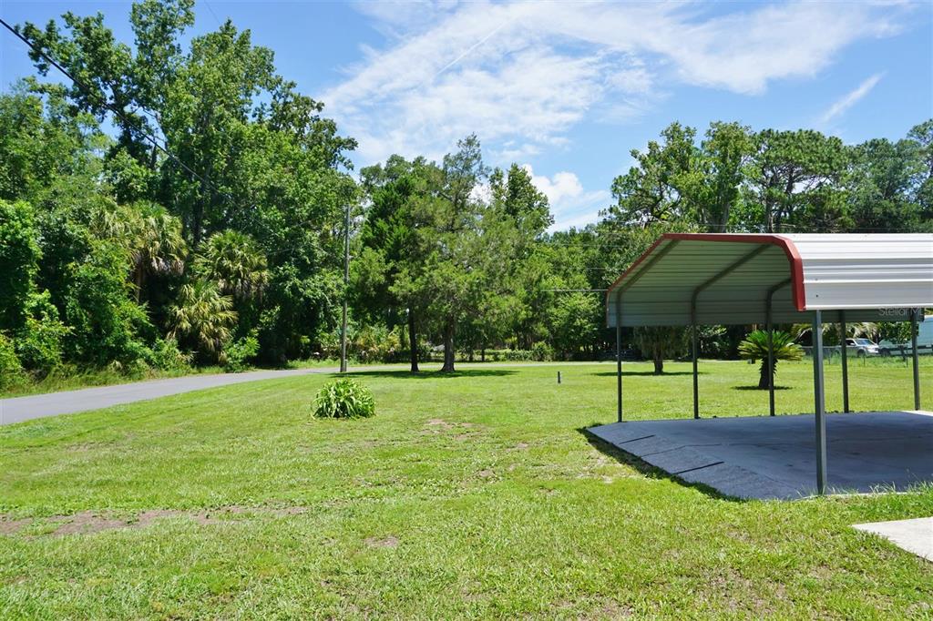 A grassy yard features a metal carport structure on a concrete pad near a road — 405 S CAMELLIA AVENUE, CRYSTAL RIVER, FL