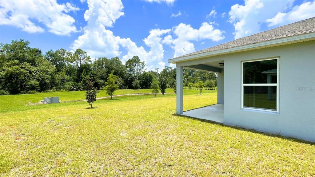 A view of a house exterior with a covered patio and a large grassy backyard — 16308 WINDING PRESERVE CIRCLE, CLERMONT, FL