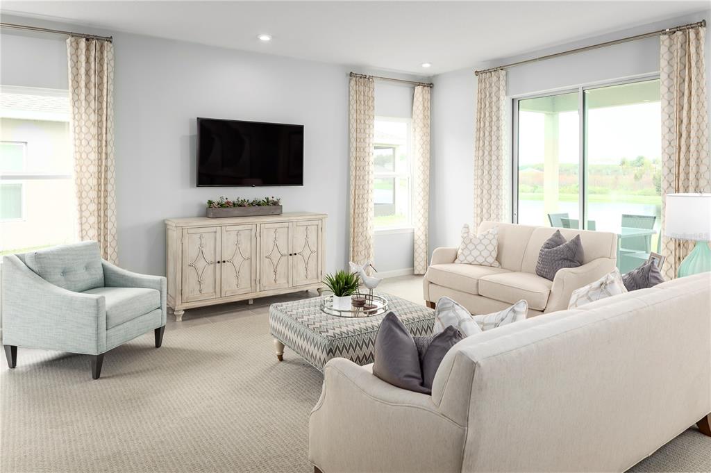 A living room features a television, a light-colored sofa, an armchair, and a patterned ottoman — 2439 WHITE LADYFISH ROAD, WIMAUMA, FL