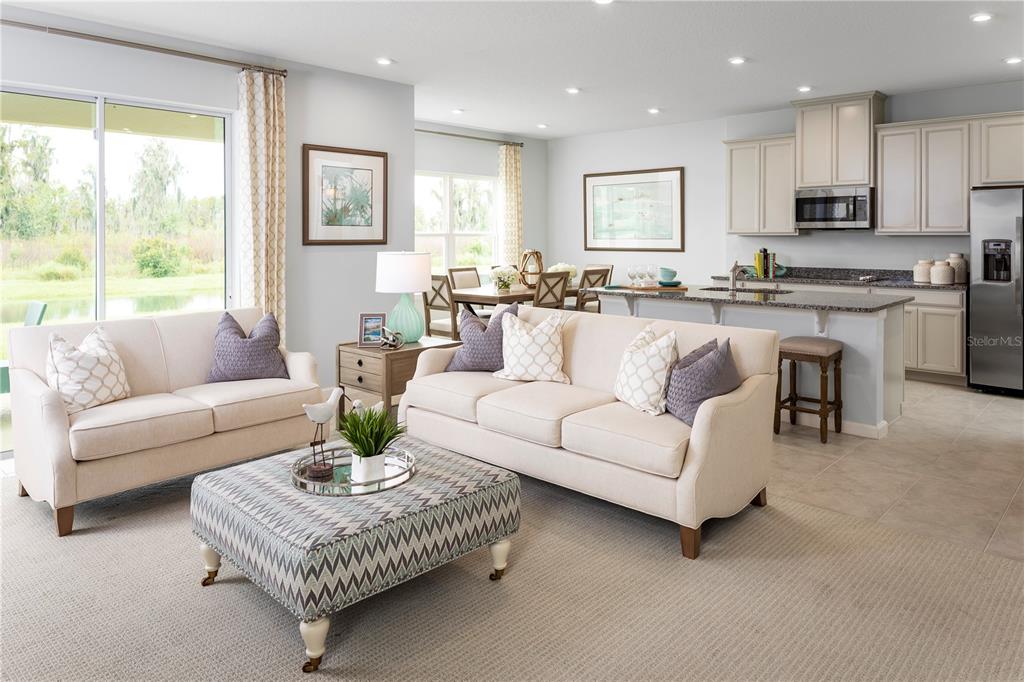A living room with beige sofas and a patterned ottoman opens to a kitchen area — 2439 WHITE LADYFISH ROAD, WIMAUMA, FL