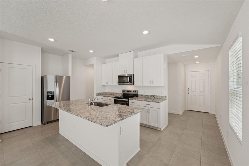 A modern kitchen features white cabinets, granite countertops, a center island, and stainless steel appliances — 104 WANDERING CREEK WAY, PALM COAST, FL