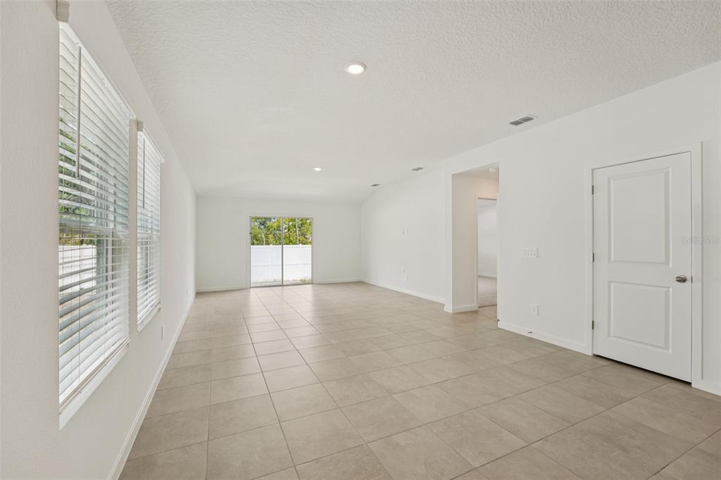 A bright, empty living room features light-colored tile flooring, white walls, and sliding glass doors — 104 WANDERING CREEK WAY, PALM COAST, FL