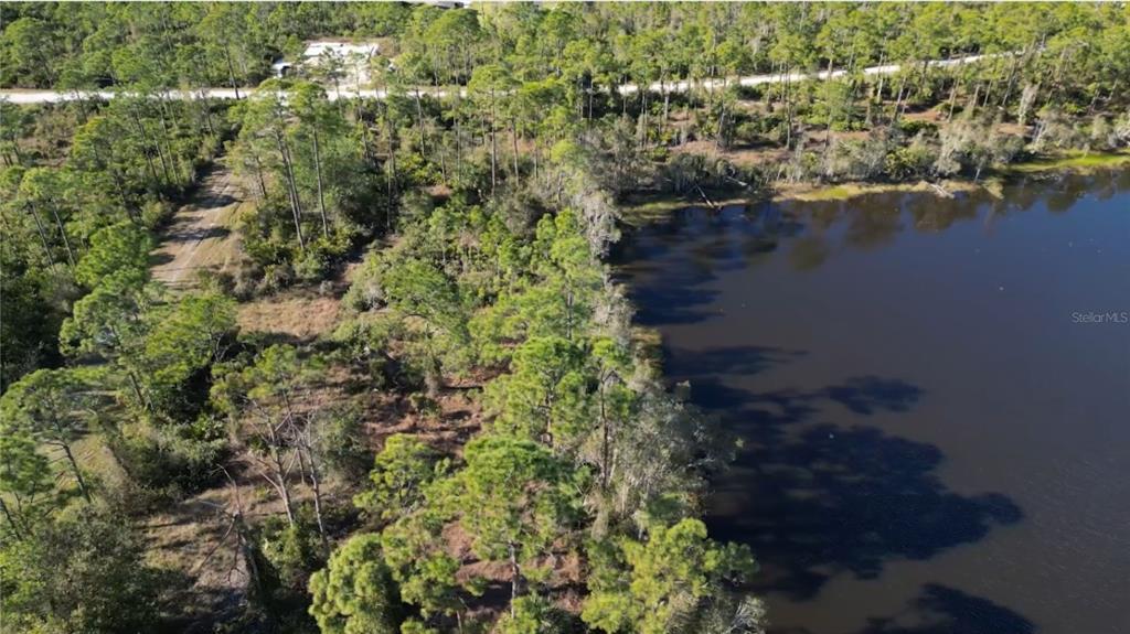An aerial view shows a wooded lot bordering a dark lake with a dirt path — 12135 LUDDEN COURT, PUNTA GORDA, FL