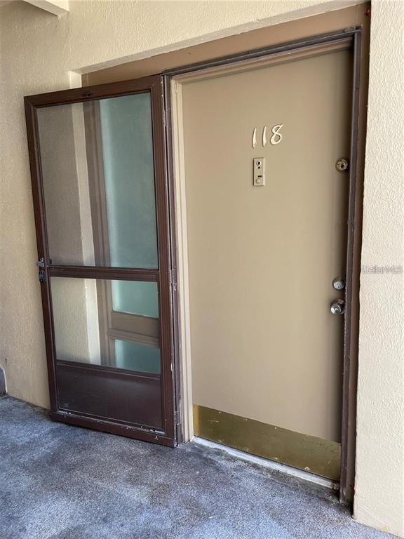 An exterior view of a tan apartment door numbered 118 with a brown screen door — 586 ORANGE DRIVE UNIT 118, ALTAMONTE SPRINGS, FL