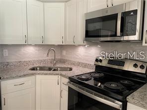 A kitchen with white cabinets, granite countertops, a stainless steel microwave, and a black stove — 586 ORANGE DRIVE UNIT 118, ALTAMONTE SPRINGS, FL