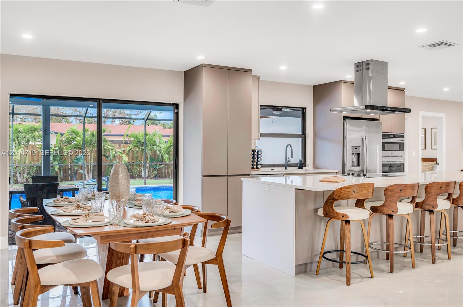 A modern kitchen and dining area feature light cabinetry, a central island, and pool views — 1111 NW 70th Ter, Plantation FL 33313, PLANTATION, FL