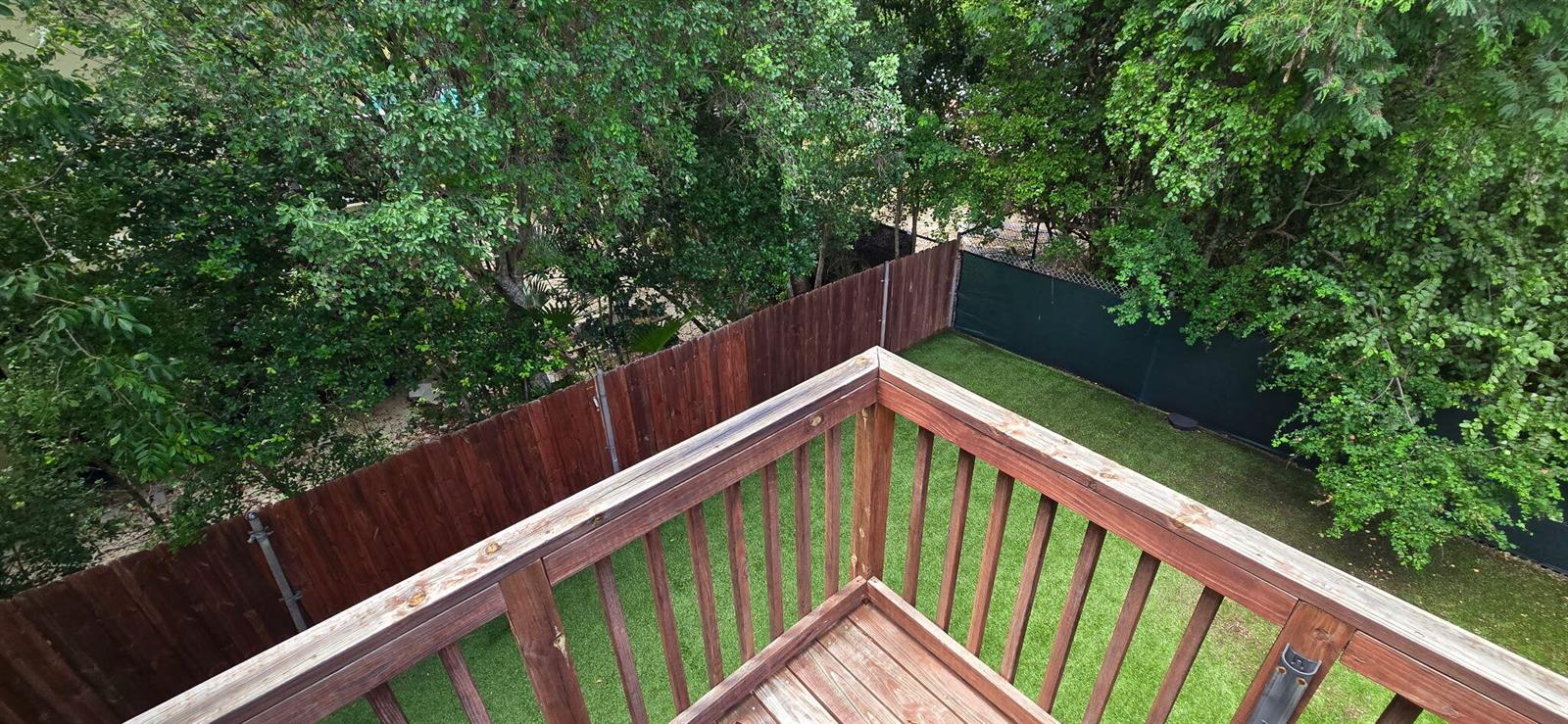 A wooden balcony overlooks a fenced backyard with green grass and surrounding trees — 410 Coconut Drive, Key Largo FL 33037, KEY LARGO, FL