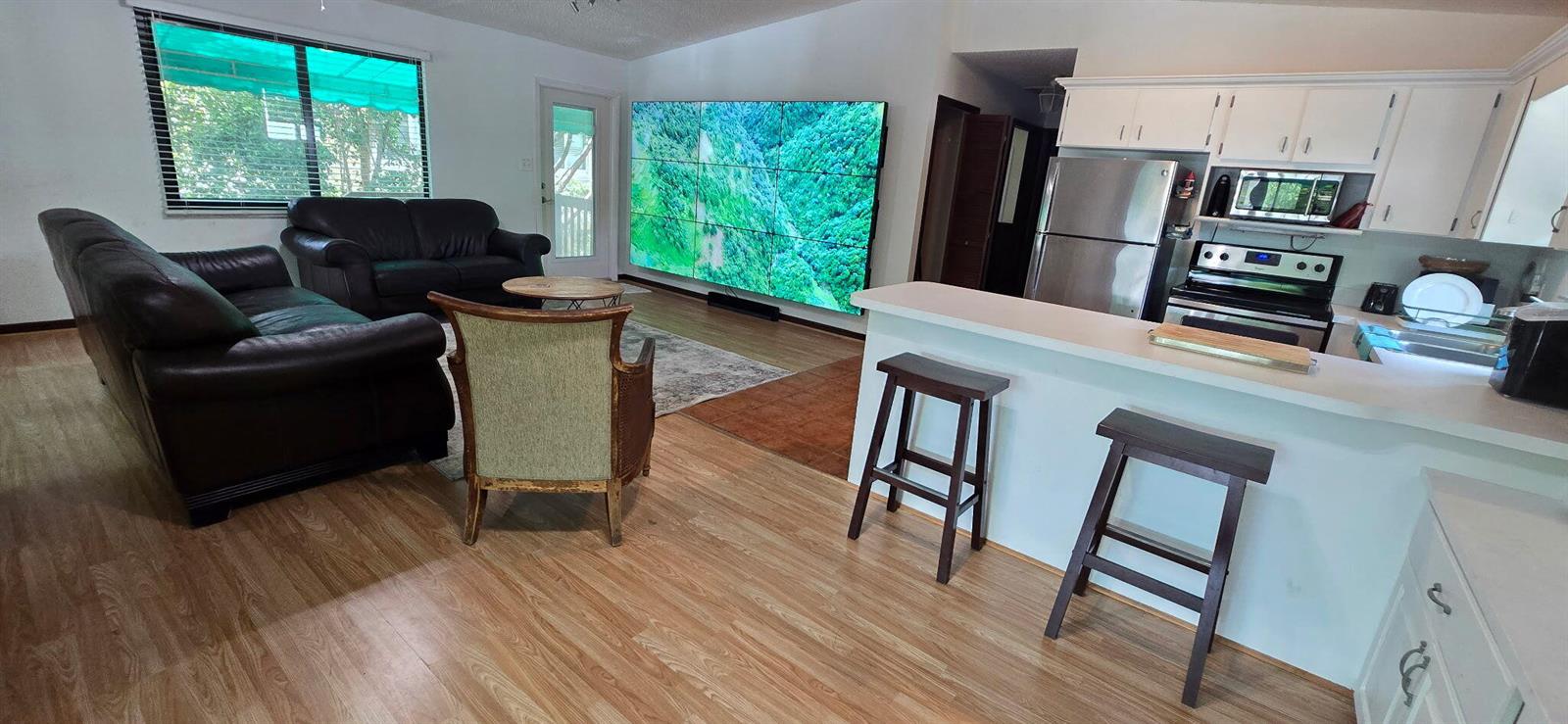 A living room with wood-look flooring, leather sofas, and a large multi-panel wall display — 410 Coconut Drive, Key Largo FL 33037, KEY LARGO, FL