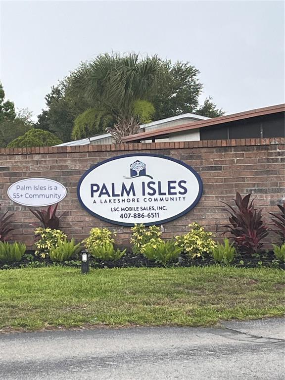 A brick wall displays a sign for the Palm Isles 55+ community with landscaping below — 1504 HAWAIIAN PALM LANE, APOPKA, FL