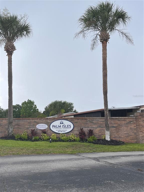 A brick wall with a Palm Isles community sign stands between two tall palm trees — 1504 HAWAIIAN PALM LANE, APOPKA, FL