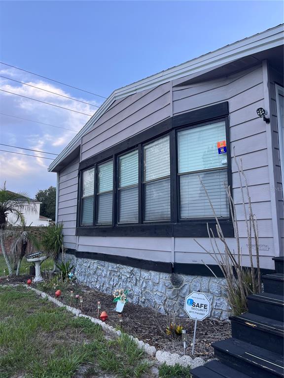 A side view of a light-colored mobile home with black-trimmed windows and stone skirting — 1504 HAWAIIAN PALM LANE, APOPKA, FL