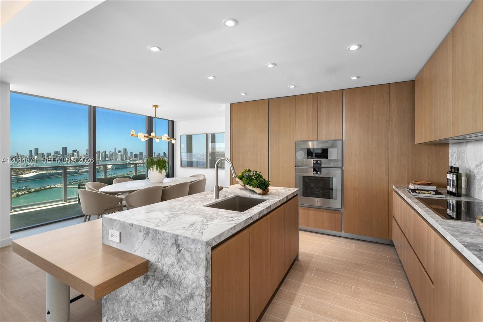 A modern kitchen features a marble island, wood cabinetry, and a dining area with city views — 501 West Ave # 4102, Miami Beach FL 33139, MIAMI BEACH, FL