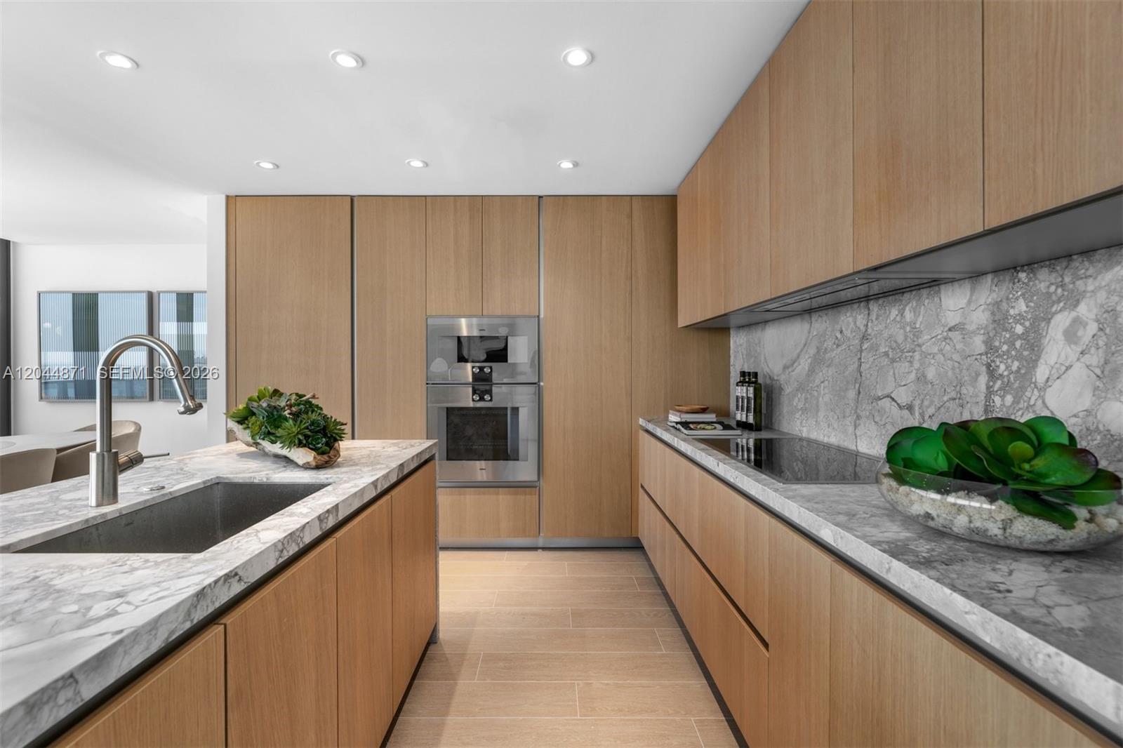 A modern kitchen features light wood cabinetry, marble countertops, and a central island with sink — 501 West Ave # 4102, Miami Beach FL 33139, MIAMI BEACH, FL
