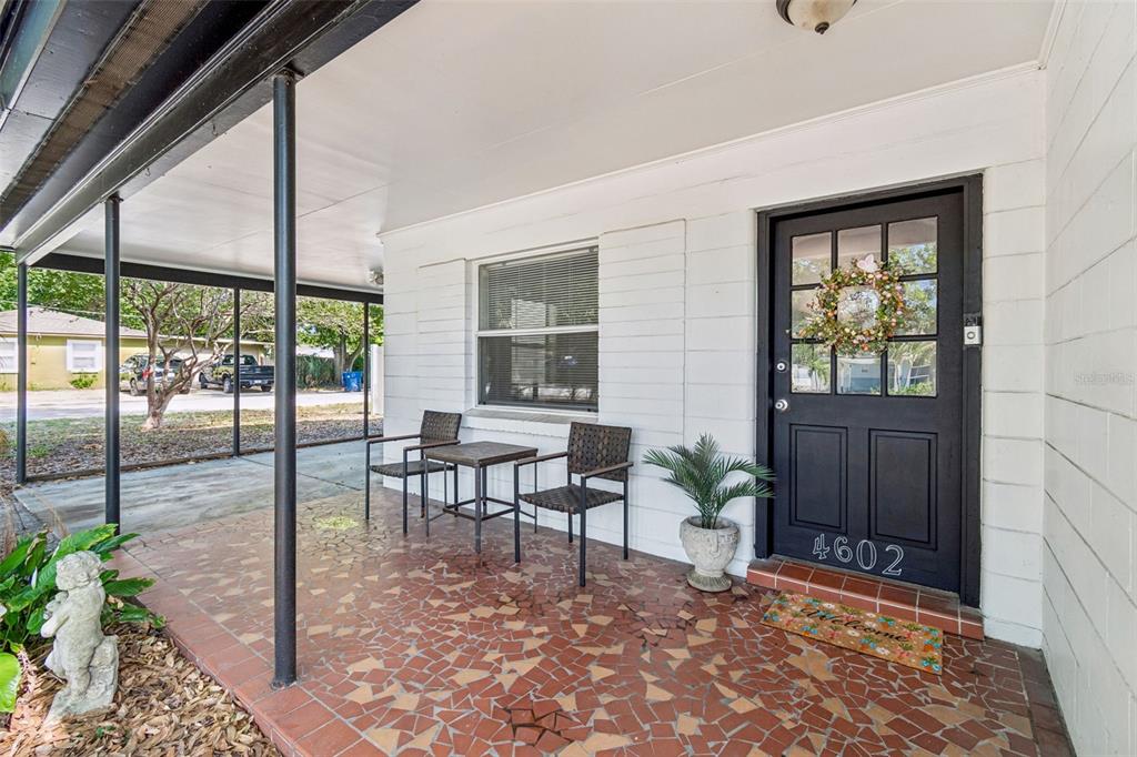 A covered front porch features a tiled floor, two chairs, a small table, and a door — 4602 W BAY VILLA AVENUE, TAMPA, FL